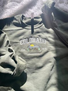 Colorado, stand up! Comfy sweatshirt with Colorado in a varsity-like font featuring a mountain design. This pullover Crewneck will keep you stylish and warm with its fleece lined fit.  You can add names on the sleeve for $5 extra!  This sweatshirt is available in 6 colors:  ✨ Military Green ✨ Sand ✨ White ✨ Light Blue ✨ Navy (words will be in white) ✨ Heather Gray If there is a color you have in mind other than the ones available, send me a message and I can help! -Sweatshirt brand: Gildan -Size Trendy College Sweatshirt With Embroidered Graphics, Varsity Style Campus Top With Letter Embroidery, Casual Green Sweater With Embroidered Graphics, Embroidered Graphics Crew Neck Top, Crew Neck Tops With Embroidered Graphics For Campus, Green Crew Neck Top For Campus, Crew Neck Embroidered Graphics Tops For Campus, School Spirit Crew Top With Embroidered Graphics, Casual Green Sweatshirt With Embroidered Graphics