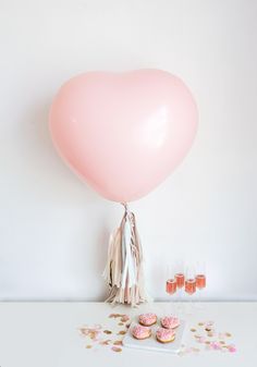 a pink heart shaped balloon with tassels and confetti on the table