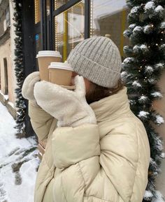 a woman holding a cup of coffee in front of a building with snow on the ground