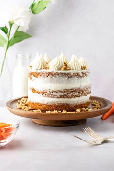 a carrot cake sitting on top of a wooden plate next to a vase with flowers