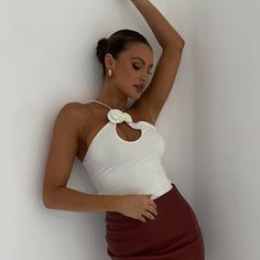 a woman leaning against a wall wearing a white top and maroon skirt with her hand on her head