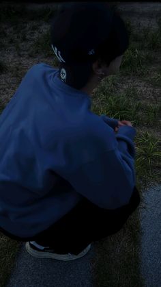 a young man sitting on the ground looking at his cell phone while wearing a blue jacket