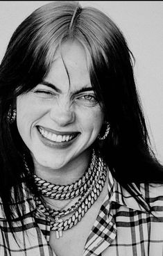 a black and white photo of a woman with long hair wearing necklaces, smiling