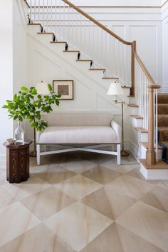 a living room with white walls and wooden floors, a beige couch and some stairs