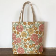 a large floral print bag sitting on top of a wooden table next to a white wall