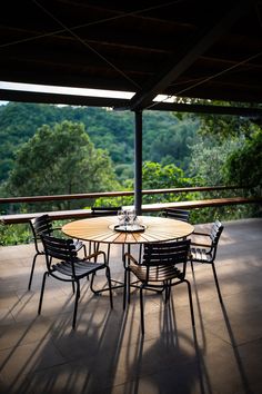 an outdoor table and chairs on a patio overlooking the trees in the distance with sunlight streaming through the roof