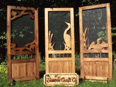 three wooden doors sitting in the grass near each other with carved birds on them and trees behind them