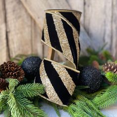 a black and gold striped ribbon with pine cones on the side next to evergreen branches