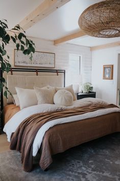 a large bed sitting under a window next to a plant in a room with white walls