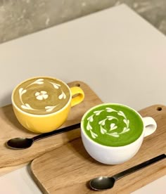 two cups of green and yellow soup on wooden serving trays