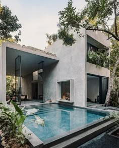 an outdoor swimming pool in front of a house with trees and bushes around it, surrounded by greenery