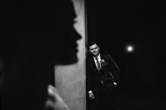 a black and white photo of a man in a suit looking at his own reflection