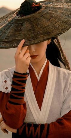 a woman wearing a large hat and holding her hand to her face while standing in the desert