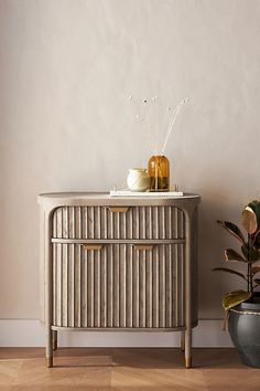 a white cabinet sitting next to a potted plant on top of a hard wood floor