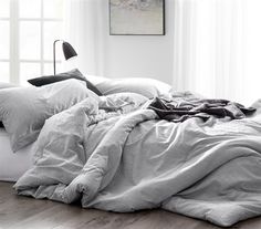 an unmade bed with white sheets and pillows in a room next to a window