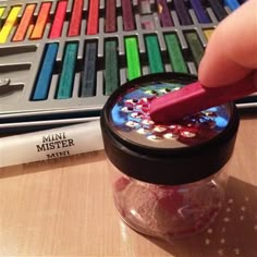 a person is holding a pink brush in front of a jar full of colored crayons