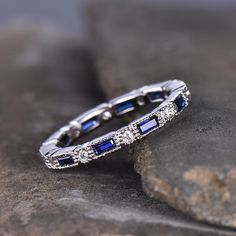 a diamond and blue sapphire wedding ring sitting on top of a rocky surface with rocks in the background