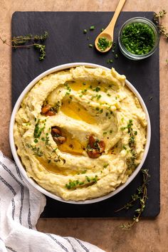 mashed potatoes in a white bowl with green herbs and a wooden spoon next to it