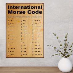 an international morse code poster hangs on the wall next to a vase with flowers in it