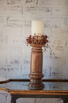 a white candle sitting on top of a wooden table next to a brick wall and metal frame