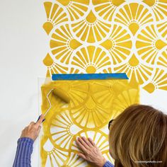 a woman is painting an art piece on the wall with yellow paint and white stencils