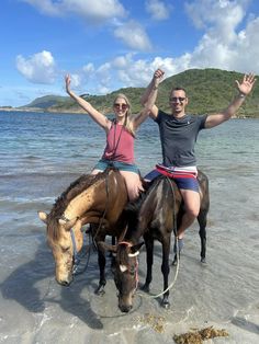 two people riding horses on the beach with their arms in the air and one person standing next to them