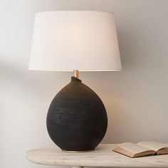 a black vase sitting on top of a table next to a white lamp and an open book