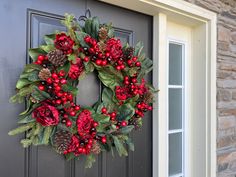 a wreath on the front door of a house with red berries and pineconis