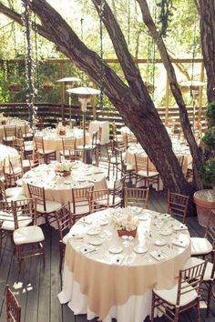 tables and chairs are set up for an outdoor wedding reception under a tree with hanging lights