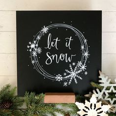 a black sign that says let it snow next to some christmas decorations and pine cones