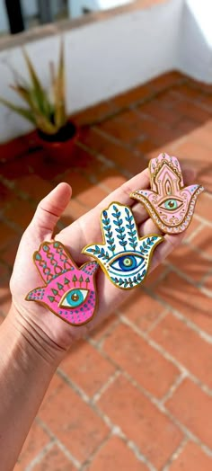 a person's hand holding three different colored hamsah and an eye shaped brooch