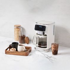 a coffee maker sitting on top of a counter next to two cups and a tray