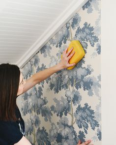 a woman is cleaning the wall with a yellow sponge on it and she's looking at the wallpaper