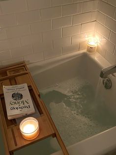 a candle is lit next to a book in a bathtub with soap and water