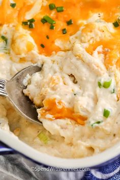 a spoon full of mashed potatoes with cheese and green onions on top in a white bowl