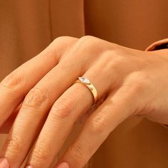 a woman's hand wearing a gold ring with a diamond on the middle finger