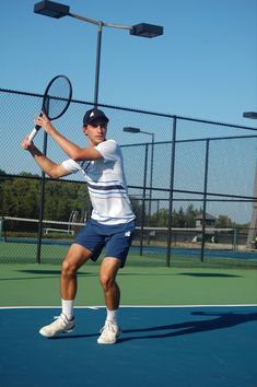 a man holding a tennis racquet on top of a tennis court in front of a fence