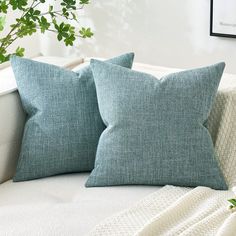 two blue pillows sitting on top of a white couch next to a potted plant