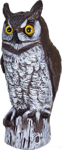 an owl figurine with yellow eyes sitting on top of a tree stump in front of a white background