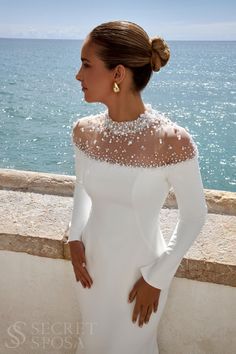 a woman in a white dress standing by the ocean with her hands on her hips