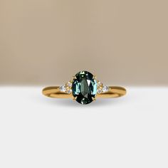 an oval cut green and white diamond ring with two diamonds on each side, set in yellow gold