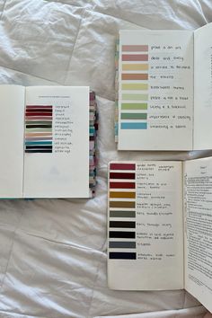 three books with different colors on them sitting on a bed next to an open book