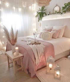 a white bed with pink sheets and pillows in a bedroom next to a window filled with lights