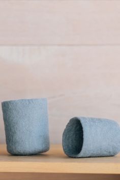 two blue felt cups sitting on top of a wooden table next to a vase filled with flowers