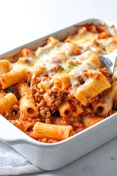 a white casserole dish filled with pasta and meat covered in sauce, topped with a fork