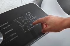 a hand is pointing at the controls on a washer that has buttons and symbols