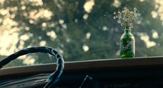 a green bottle sitting on the dashboard of a car next to a window with trees in the background