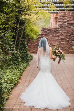 a woman in a wedding dress walking down a brick path with her veil pulled back