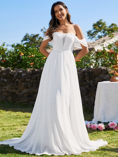 a woman in a white wedding dress standing on the grass with her hands on her hips