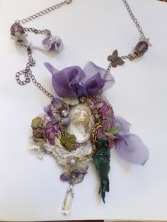 Intricated fairy fantasy spring necklace with a cabochon, an elf is watching at some flowers and butterflies all around the necklace, I worked on a metal silver base with silk chiffon, velvet, tulle, ceramic butterflies, the silk is dye, many colors and rhinestones , beads and crystal for this intricated necklace which is a tribute to the nature, the details are stunning, light, not heavy, we attach the necklace with a beautiful silk chiffon, another part in metal with violet bairies on the top Ceramic Butterflies, Fantasy Elf, Spring Necklace, Cabochon Necklace, Flowers And Butterflies, An Elf, Silk Chiffon, Fairy Garden, Jewelry Necklace Pendant